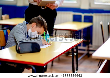 Elementary schoolchild writing at the desk in the classroom. Education during epidemic.