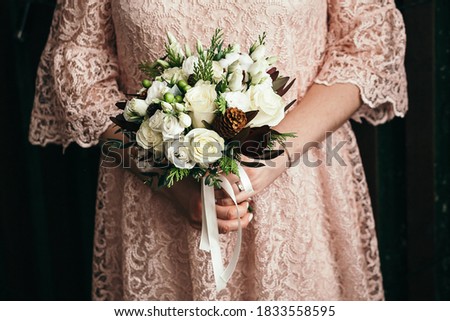 Bridal bouquet, hold the wedding bouquet in your hand, satin ribbons adorn the wedding bouquet of roses, on the background of the bride's dress, fresh flowers, made by a florist