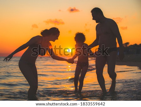 Dark silhouette of a happy family on a sunset.Father, mother, baby son walking along the sandy beach.Family having fun on the beach.Travel lifestyle, parents, dad with children on summer vacation.