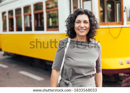 Woman with curly hair in a dress walking in Lisbon, yellow tram on the background