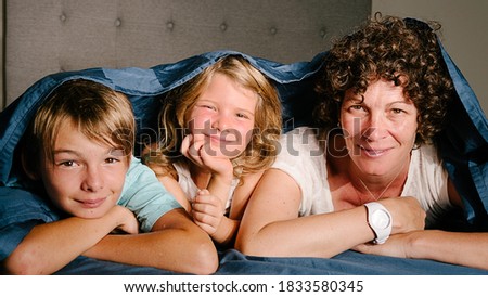 Stock photo of young mother and her kids looking at camera while lying in bed.
