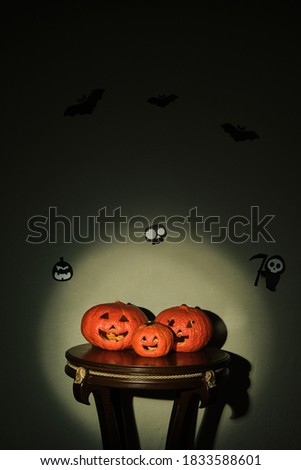 Colored pumpkins on wooden stool in front of a black backdrop. with carved figures on it.
