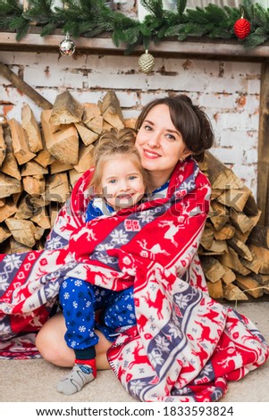 New Year's portrait of mother and child. mother wrapped the child in a blanket, the girl laughs, mother hugs her daughter. Firewood lies in a fireplace, which is decorated with New Year's toys