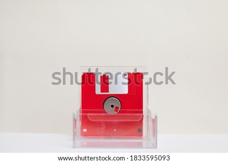 Red floppy disk in a transparent box on a white background. 1990s style.
