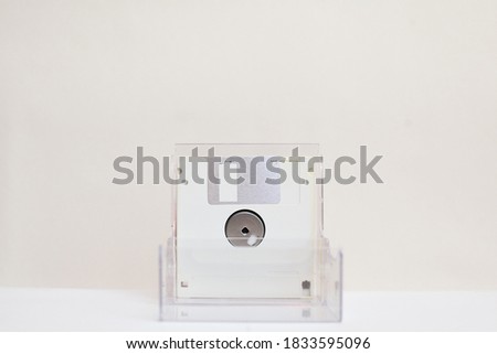 Green floppy disk in a transparent box on a white background. 1990s style.