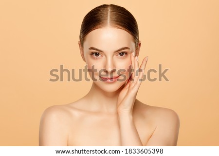 Portrait of young beautiful woman with brown eyes and glowing skin, isolated on beige background. Skincare concept