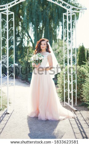 Happy caucasian fiancee keeping bouquet of flowers and wearing white dress. Concept of bridal photo session and wedding.