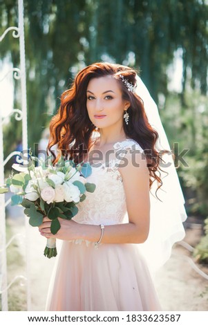 Happy caucasian fiancee keeping bouquet of flowers and wearing white dress. Concept of bridal photo session and wedding.