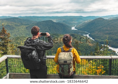 Hikers couple camping walking with backpacks in Quebec National Park taking picture of view with phone in Autumn, Canada forest travel lifestyle. Tourists looking at Jacques Cartier National Park.