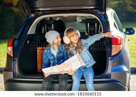 Agreeable boy and girl looking at the road map while sitting in the auto's trunk and discussing the move direction. Royalty-Free Stock Photo #1833660115
