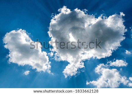 White cumulus clouds and a blue sky with sun rays
