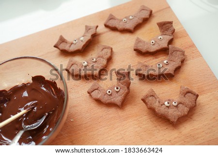 Halloween sweets cookies baked in bats shape laying on a wooden cutting board with chocolate