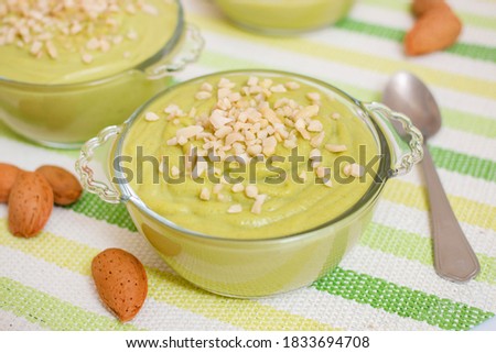 Fresh and sweet avocado pear cream dessert with little pieces of almond on top on glass bowls.