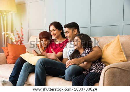 Indian family sitting on sofa and using smartphone, laptop or tablet, watching movie or surfing internet Royalty-Free Stock Photo #1833733024