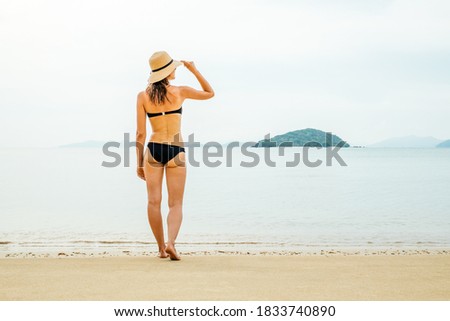 Beautiful woman in sunhat and bikini standing at the beach