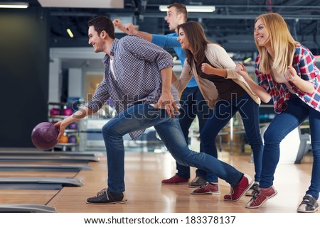 Friends cheering their friend while throwing bowling ball  