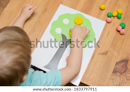 Boy is playing with a model. Glue colored apples and glue on wood. Montessori materials. Development, education. Preschool children educational toys. Activity at home.