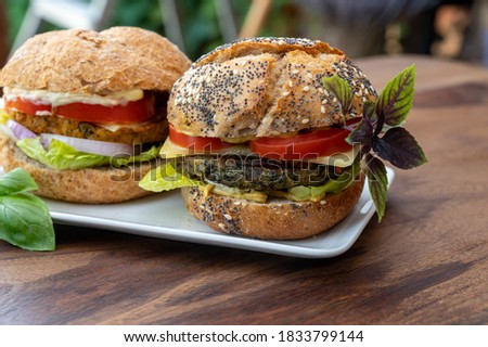Eating of fresh and healthy vegetarian hamburgers with grilled spinach or pumpkin burgers, organic buns and vegetables close up