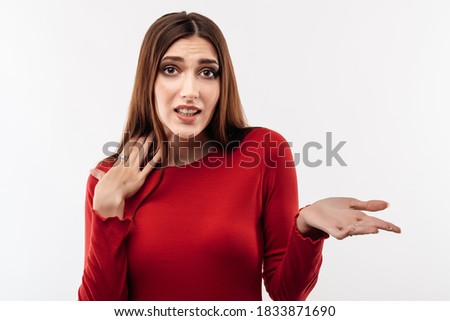 Young shocked woman with long chestnut hair, wearing in casual red sweater expressing surprise on camera. Human emotions, facial expression concept. Studio shot, white background