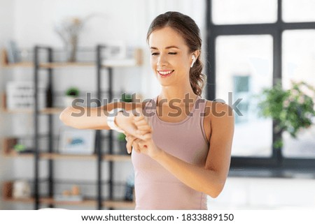 sport, fitness and technology concept - happy smiling young woman with smart watch and earphones exercising at home