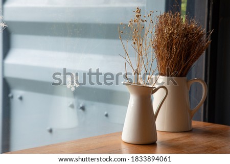 Selective focus and close up shot of cafe decorating with dried flowers in white ceramic jar on the wooden table near the glass window with snowflake decoration shows minimal style with copy space.