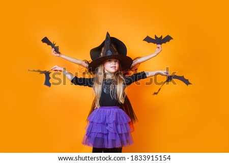 Two little girls in halloween costumes having fun on orange background