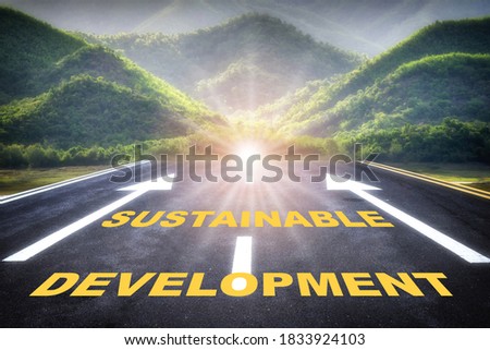 Sustainable development words with white arrow sign marking on road surface for giving directions on mountain background. Sustainability industry, ecosystem and healthy environment concept background