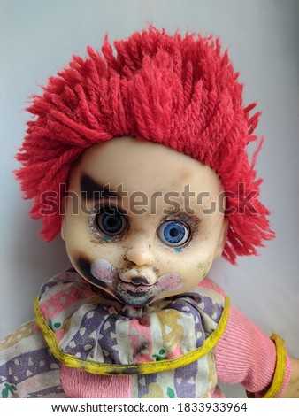 scary and old battered clown doll with burnt face and red hair on the white background