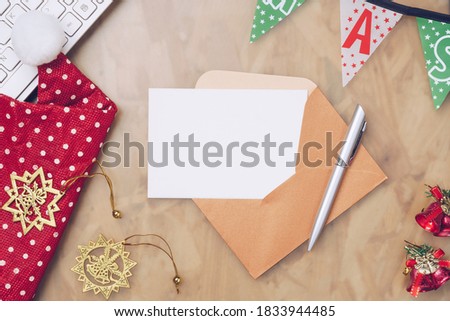 Mockup blank Christmas Card and gold brown envelope with Christmas decorations. Xmas  ornaments on home office table, top view. Holiday party workspace mock up, postcard with copy space.
