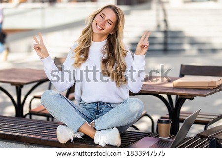 Happy woman giving the peace sign sitting in a urban bench