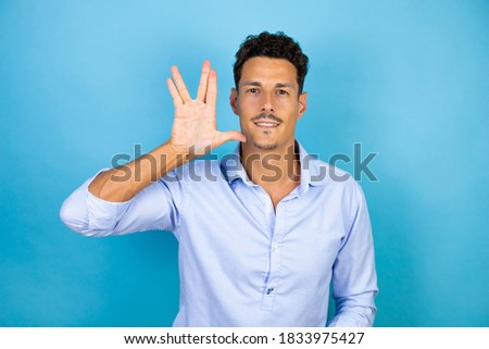 Young handsome man wearing blue shirt over isolated blue background doing hand symbol