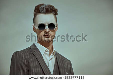 Men's fashion concept. Portrait of a handsome man in elegant suit and trendy hairstyle posing against the sky. Body painting. Makeup and cosmetics.