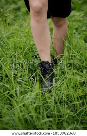 Women's feet in black leather boots walk in the tall grass. Military boots are shot close-up among the autumn grass