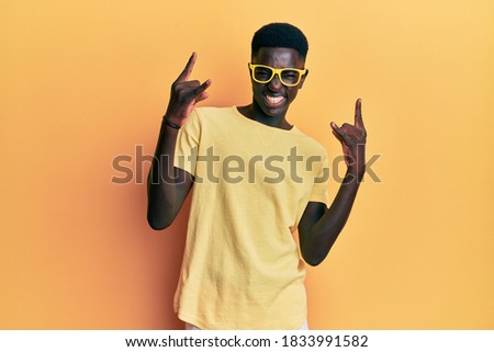 Young african american man wearing casual clothes and glasses shouting with crazy expression doing rock symbol with hands up. music star. heavy concept. 