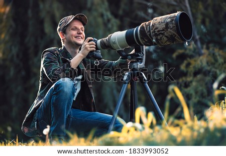 wildlife photographer using telephoto lens with camouflage coating photographing wild life using gimbal head on tripod. professional photography equipment for cinematic shooting in the nature outdoor Royalty-Free Stock Photo #1833993052