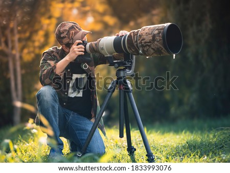 wildlife photographer using telephoto lens with camouflage coating photographing wild life using gimbal head on tripod. professional photography equipment for cinematic shooting in the nature outdoor Royalty-Free Stock Photo #1833993076