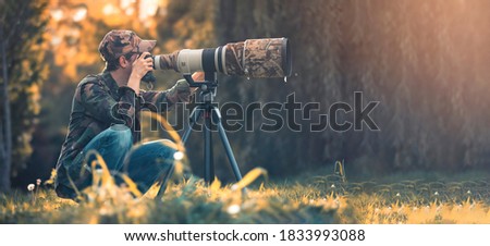 wildlife photographer using telephoto lens with camouflage coating photographing wild life using gimbal head on tripod. professional photography equipment for cinematic shooting in the nature outdoor