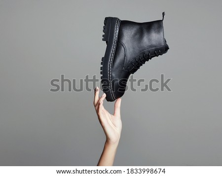 woman's hand holding Black boots in the air. fashion shoes promotion still life. stylish photo in the studio