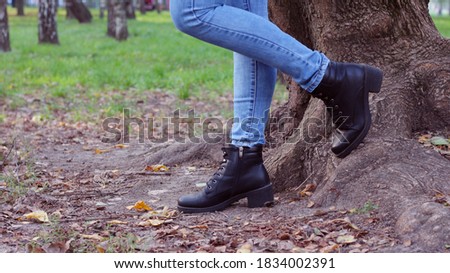 Close-up of female legs in shoes with laces and jeans near a tree trunk. Healthy lifestyle, walking outdoors in the park.
