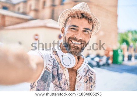 Young hispanic man on vacation wearing headphones making selfie by the camera at street of city