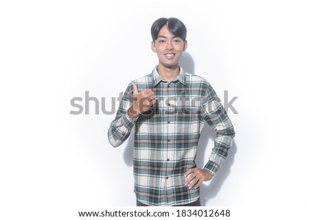 A young man wearing a plaid shirt is smiling making thumbs up sign

