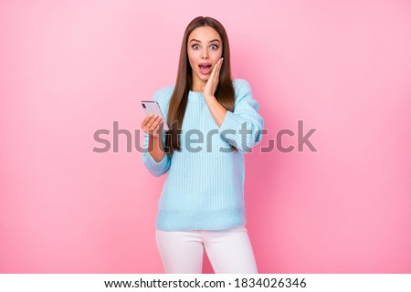 Photo of pretty shocked lady hand on cheek hold telephone check followers many likes comments wear knitted blue sweater white trousers isolated pastel pink color background