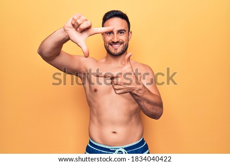 Young handsome man with beard wearing sleeveless t-shirt standing over yellow background smiling making frame with hands and fingers with happy face. Creativity and photography concept.