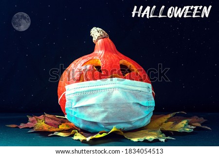 Pumpkin in a medical mask with autumn leaves on a dark background. Jack's Lantern. Halloween Decorations 2020. Coronavirus pandemic.In English the inscription "Halloween"