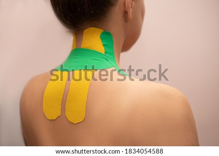 A young woman with a bright kinesiotherapy tape with on the shoulder and back at the therapist's massage salon or clinic close up Photo. Backache