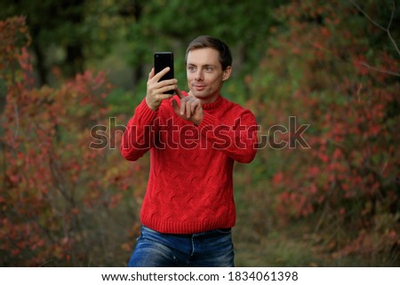 Man in red sweater enthusiastically make a photo by smartphone