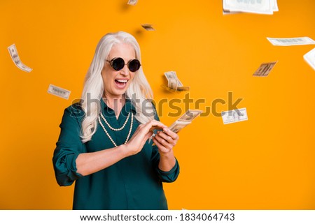 Photo of funky crazy grandma lady pack usa bucks hands money fall sky wealthy person spend money luxury wear green shirt sun specs necklace isolated bright yellow color background