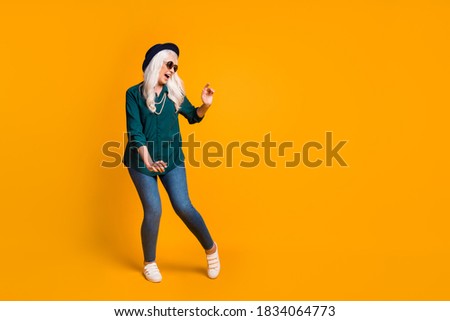Full length photo of crazy granny lady music lover senior party cool look dance youth moves wear green shirt sun specs necklace retro cap shoes isolated yellow color background