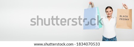 panoramic shot of pleased young woman holding shopping bags with black friday lettering on white