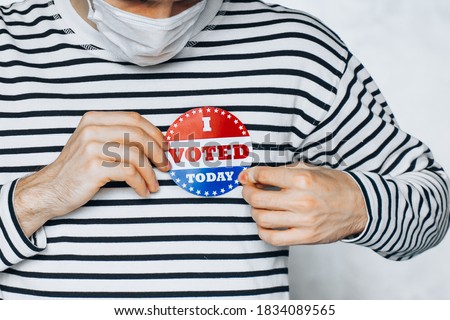 young man in face medical mask wearing on shirt I VOTED TODAY pin. election day on coronavirus pandemic. November elections in the United States 2020. Copy Space. blurred background. New normal